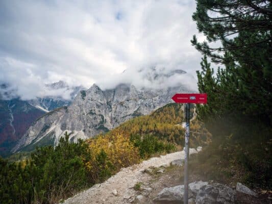 Znak planinarske kuće na stazi sa slikovitim planinskim pejzažem u pozadini.